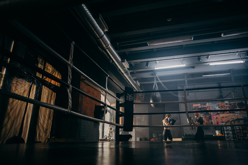 Dark photo of boxing gym with a woman boxing and a man coaching